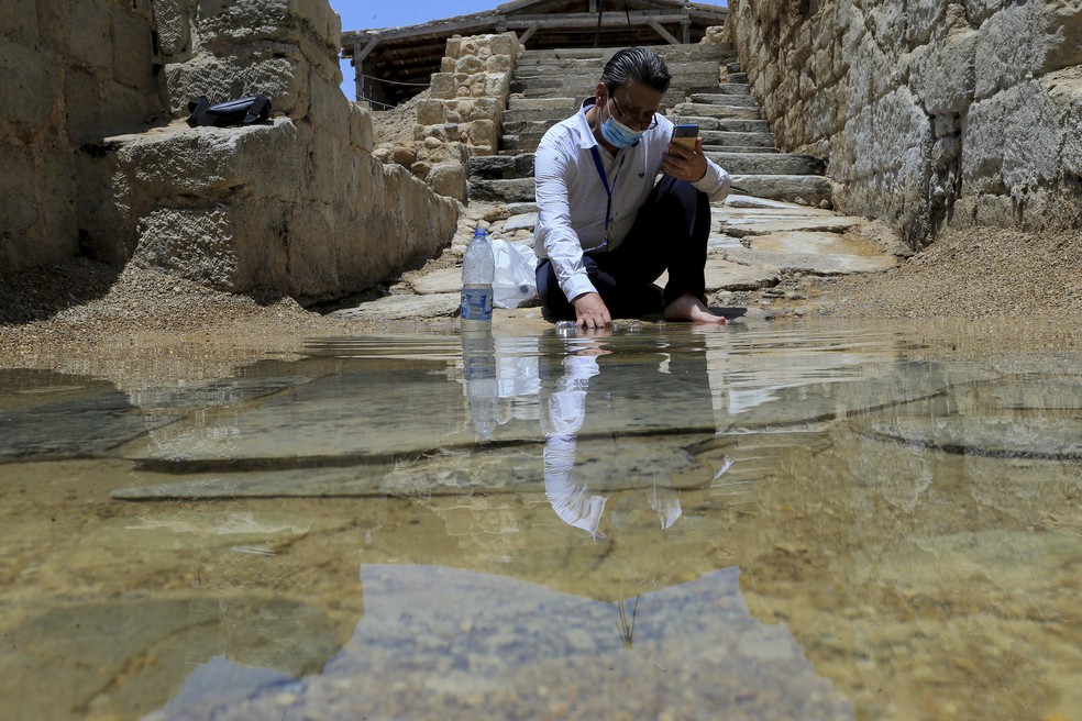 O cristão sírio Zuhair Al-Sahawi mergulha uma mão na água do local de batismo Betânia do Além-Jordão, na margem oriental do Rio Jordão, na Jordânia — Foto: Raad Adayleh/AP