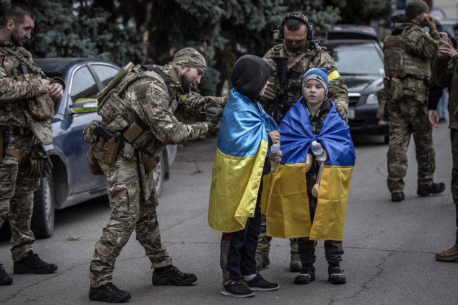 Soldado ucraniano assina uma bandeira nas costas de duas crianças em Kherson