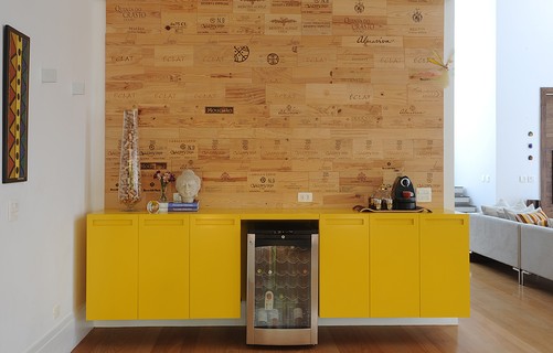 O bufê amarelo com desenho da arquiteta Luita Trench ganha destaque na frente da parede feita com caixas de vinho