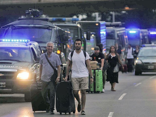 Pessoas carregam suas bagagens através de uma fila de viaturas que garantem o acesso ao aeroporto internacional Ezeiza, em Buenos Aires, na terça (22) (Foto: AFP Photo/Telam/STR)