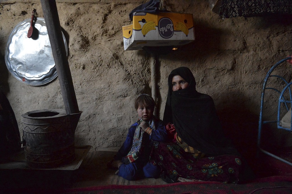 Sabehreh (à direita) e sua filha Zakereh, que está noiva do filho de 4 anos do dono da mercearia para cobrir a dívida da família, em foto tirada em 14 de outubro de 2021. Família mora no campo de pessoas deslocadas de Zaimat, em Qala- i-Naw, na província de Badghis. O casamento infantil é praticado há séculos no Afeganistão, mas a guerra, a seca e a pobreza levam famílias a vender suas filhas cada vez mais cedo. — Foto: Hoshang Hashimi/AFP