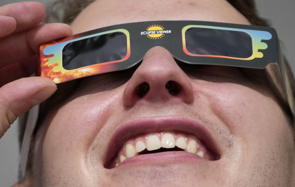 Homem usa óculos especiais para assistir eclipse em Trafalgar Square, Londres, nesta quinta-feira (10) — Foto: Frank Augstein/AP