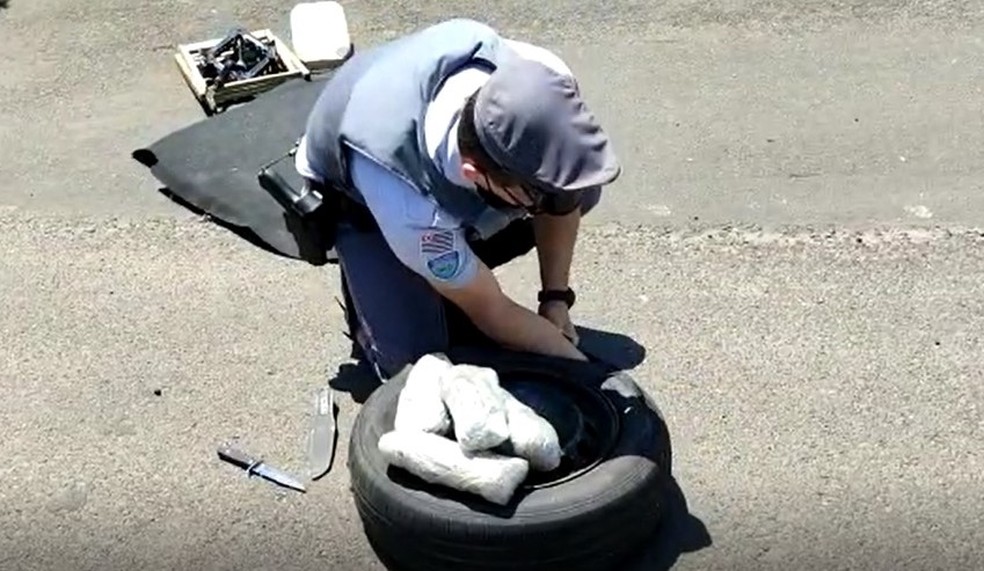 Policiais precisaram cortar o pneu do estepe com uma faca para retirar os pacotes da droga — Foto: Polícia Rodoviária/Divulgação