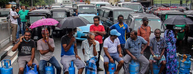 Pessoas sentadas em cilindros de gás vazios  bloqueiam estrada para protestar contra a escassez de combustível e gás de cozinha em Colombo, no Sri LankaAFP