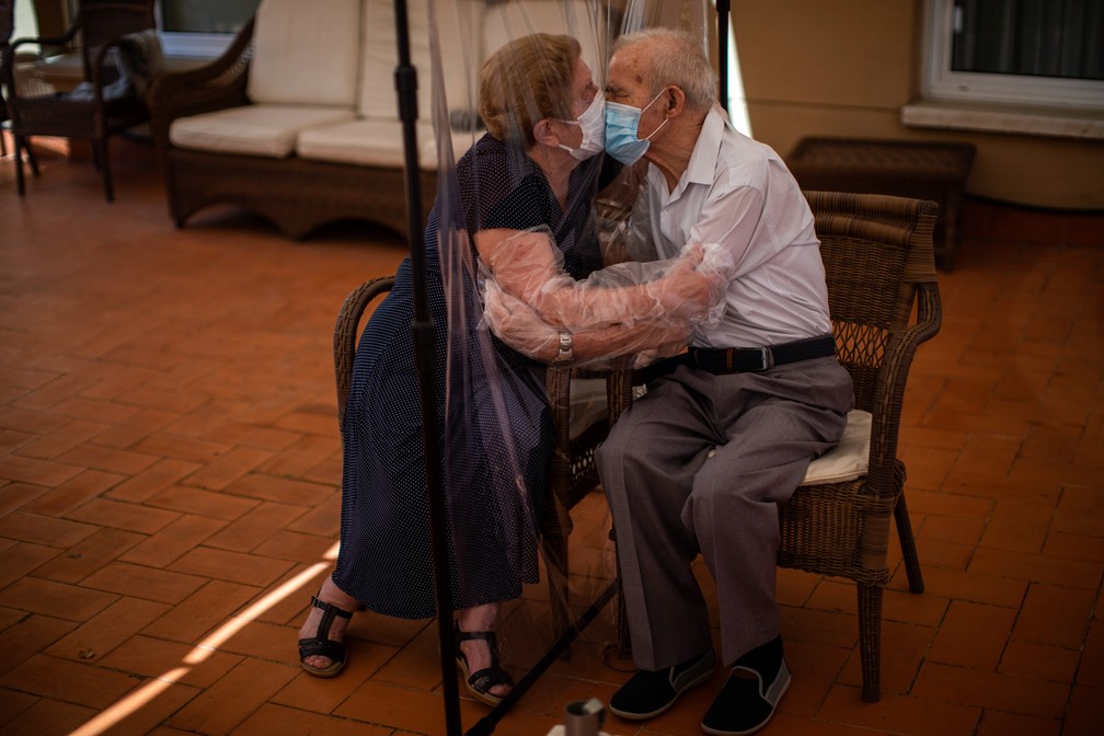 22 de junho - Agustina Canamero, de 81 anos, e Pascual Perez, de 84, se abraçam e se beijam através de uma tela de plástico para evitar a contaminação pelo coronavírus em uma casa de saúde em Barcelona, na Espanha  — Foto: Emilio Morenatti/AP