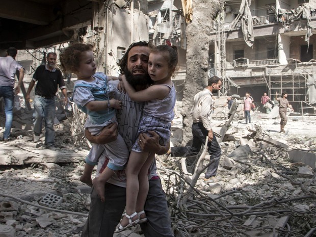 Um homem sírio carrega suas filhas sobre escombros após um atentado na Síria  (Foto: AFP Photo/Karam)