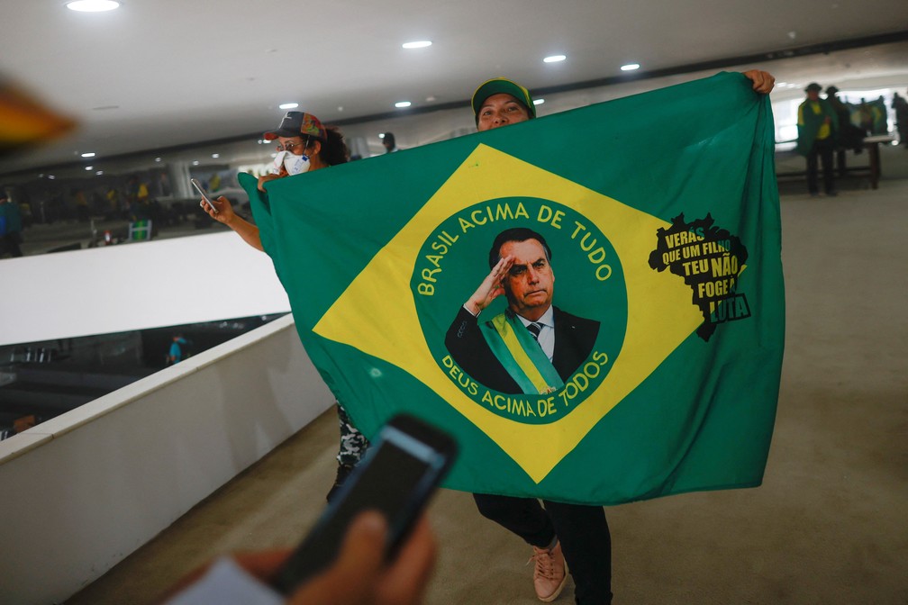 Criminosos fazem fotos com uma bandeira mostrando a imagem de Bolsonaro em continência após invasão em Brasília — Foto: Adriano Machado/Reuters