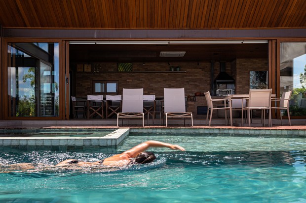 A área da piscina se integra à área gourmet graças aos enormes panos de vidro da residência, que se abrem ao quintal 