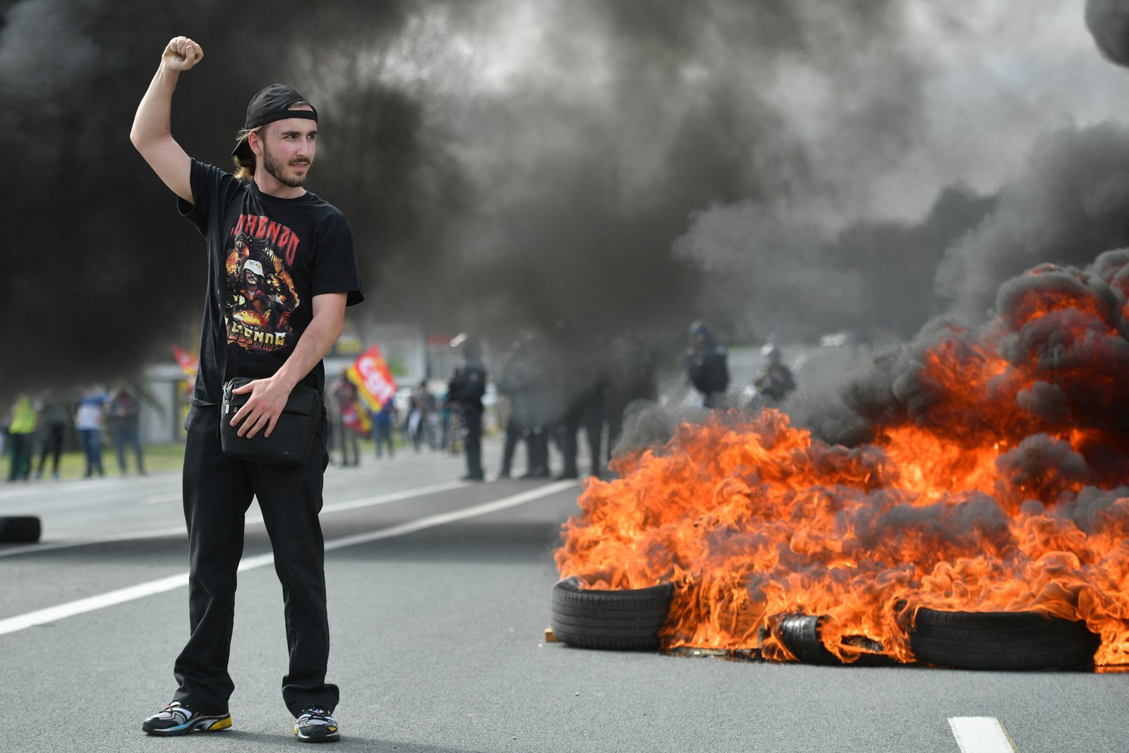Um manifestante ergue o punho no ar ao lado de um incêndio durante protesto contra a reforma da previdência na França — Foto: Gaizka Iroz/AFP