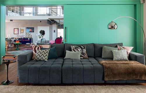 As almofadas que enfeitam o grande e confortável sofá são feitas de lenços da grife Pucci. A porta de correr verde separa o ambiente do living. Ideia da arquiteta Andrea Murao