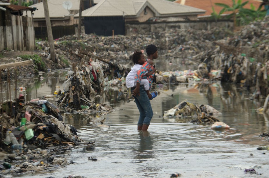 Uma menina carrega seu irmão mais novo nas costas enquanto caminham por um canal inundado em Lagos, na Nigéria