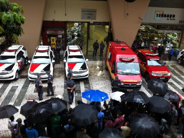 Curiosos se protegem em guarda-chuvas para acompanhar a ação policial no edifício (Foto: Paula Paiva Paulo/G1)