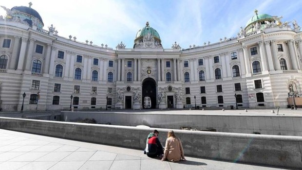 BBC - Em Viena, duas pessoas sentam em uma praça vazia. O governo austríaco proibiu reuniões de mais de cinco pessoas (Foto: HELMUT FOHRINGER / AFP via BBC)