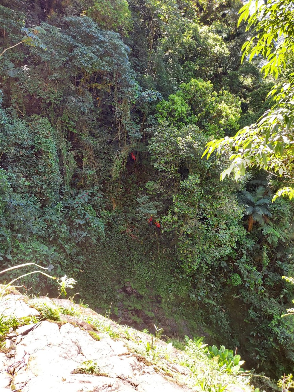 Foto tirada do possível local da queda mostra socorristas no paredão da cachoeira — Foto: GRM/Divulgação