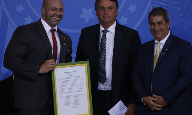 O deputado federal Daniel Silveira (PTB-RJ) exibe o indulto assinado por Bolsonaro emoldurado em um quadro ao lado do presidente e do deputado Coronel Tadeu (PL-SP) em cerimônia no Palácio do Planalto, na última quarta (27)