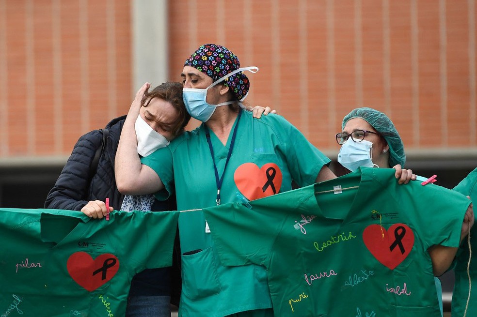 Profissionais de saúde confortam mulher de enfermeiro que morreu por cauda da Covid-19 em hospital de Leganes, perto de Madri, na sexta-feira (10)  — Foto: Pierre-Philippe Marcou / AFP