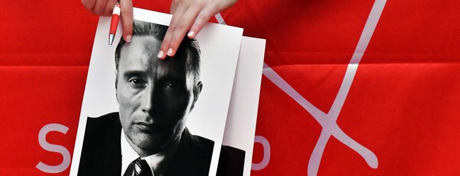 Fã segura fotos para autógrafos enquanto espera o ator dinamarquês Mads Mikkelsen no tapete vermelho da 28ª edição do Sarajevo Film Festival  — Foto: ELVIS BARUKCIC / AFP