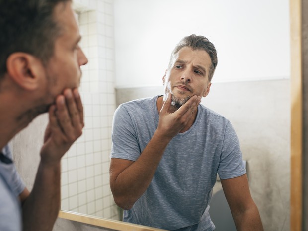 Handsome young Caucasian man checking out his beard in a bathroom mirror after a morning shave at home. (Foto: Getty Images)