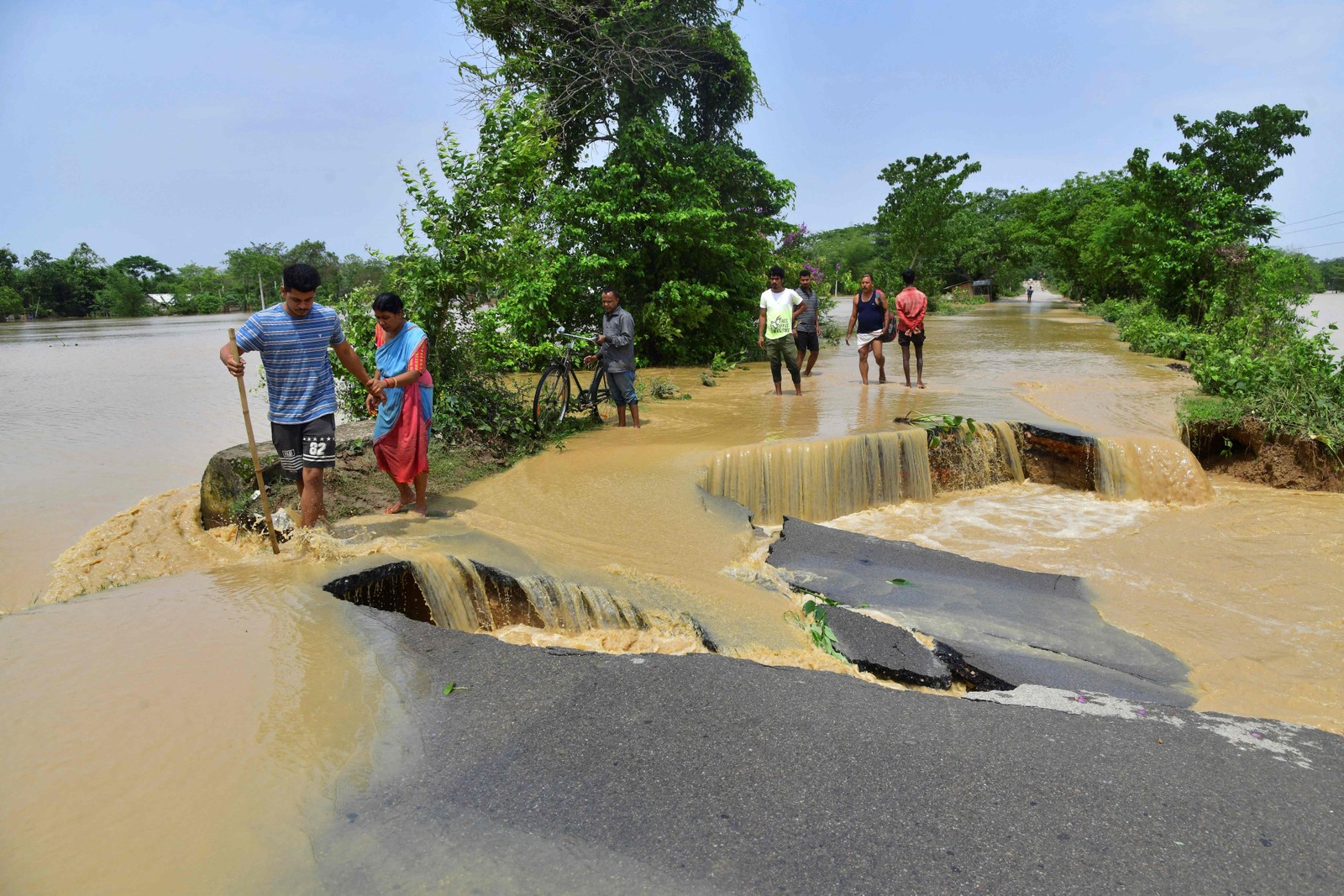 Pessoas atravessam uma estrada danificada pelas águas da enchente após fortes chuvas no distrito de Nagaon, estado de Assam, em 19 de maio. — Foto: Biju BORO / AFP