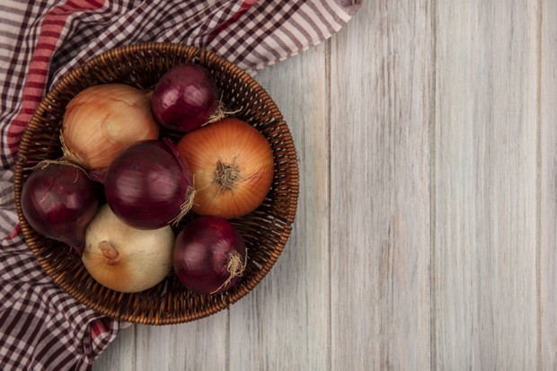 top view of healthy red and white onions on a bucket on a checked cloth on a grey wooden background with copy space (Foto: Freepik)