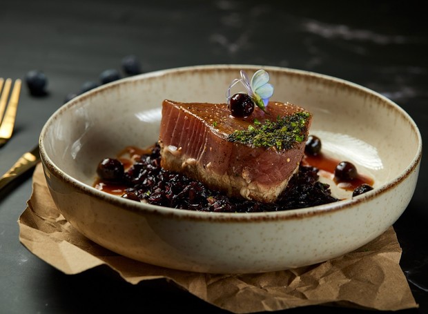 Sirva o atum selado sobre o arroz negro e finalize com molho, mirtilos, flores comestíveis e nirá (Foto: Rodolfo Regini / Divulgação)