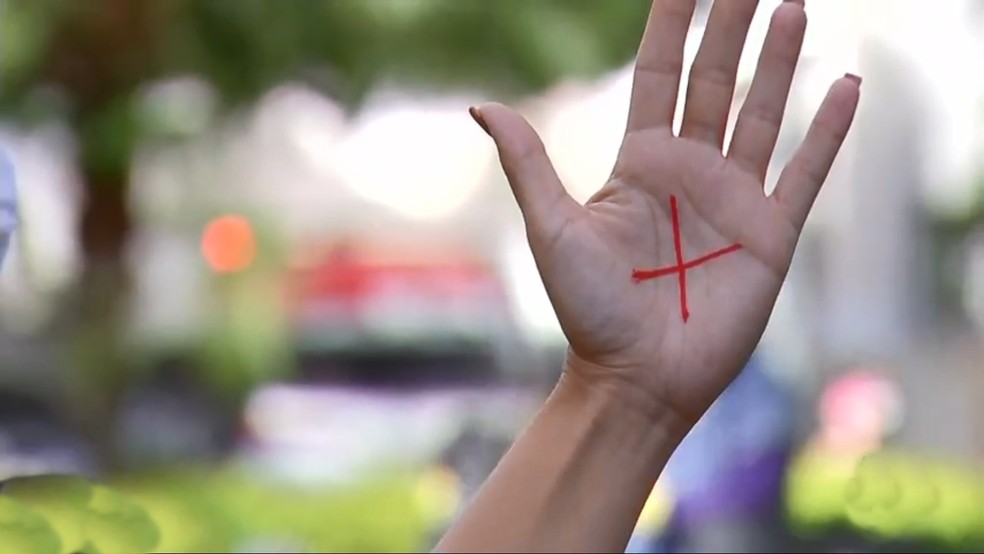 Mulher faz um X vermelho na mão para denunciar agressão — Foto: TV Globo/ Reprodução