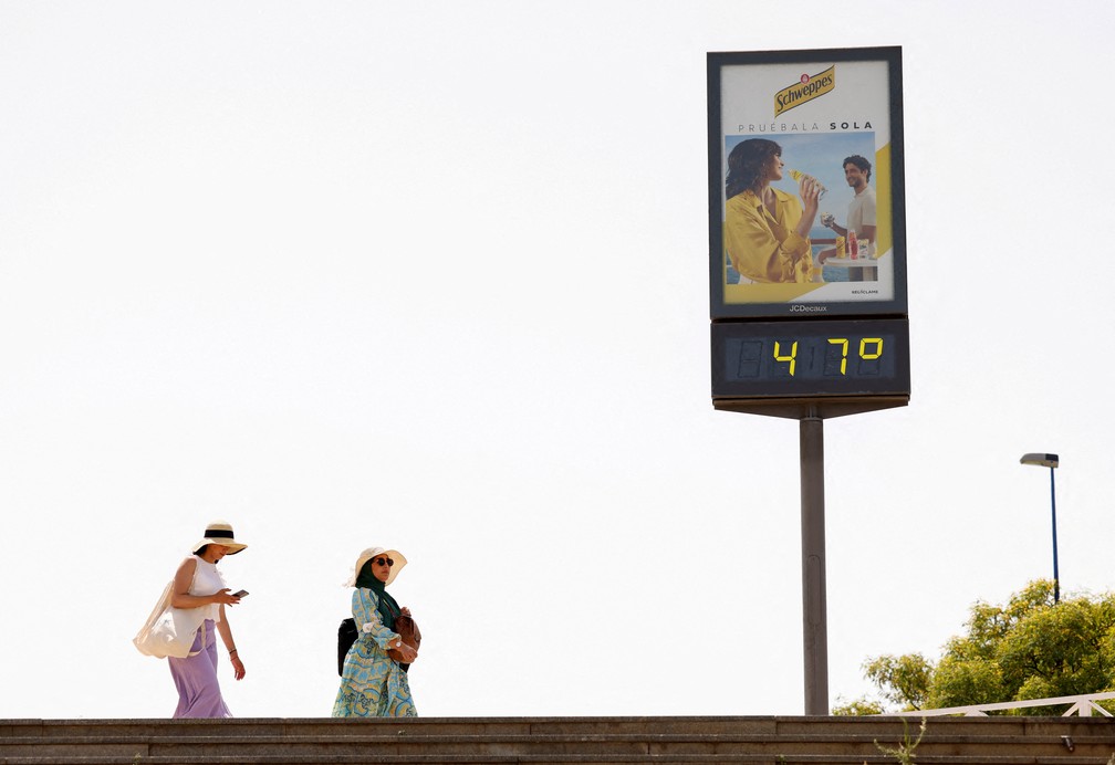Mulheres caminham ao lado de um termômetro marcando 47 graus Celsius durante a primeira onda de calor do ano em Sevilha, Espanha (11/06/22). — Foto: REUTERS/Marcelo del Pozo/File Photo