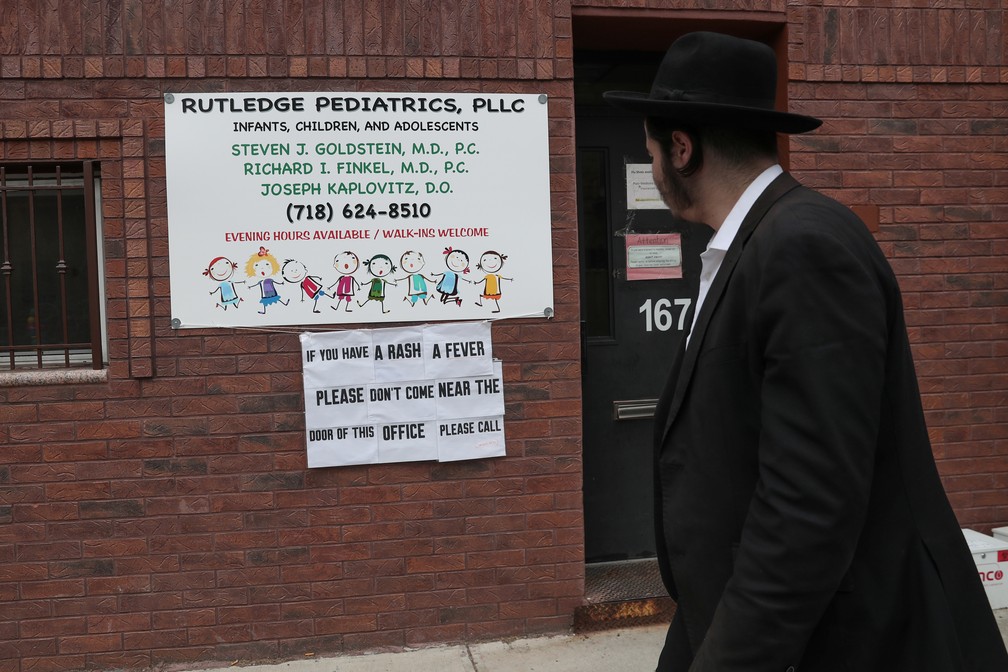 Aviso pede que pessoas com febre ou manchas vermelhas no corpo nÃ£o se aproximem de consultÃ³rio pediÃ¡trico na comunidade judaica ultra-ortodoxa de Williamsburg, em Nova York â€” Foto: REUTERS/Shannon Stapleton