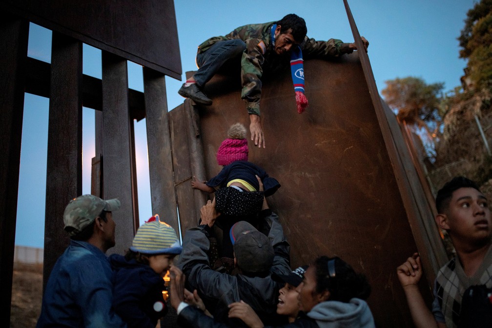 Migrantes levam crianÃ§as para pular a cerca de fronteira do MÃ©xico com os EUA nesta segunda-feira (4) â Foto: Alkis Konstantinidis/Reuters