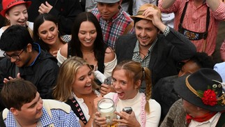 Visitantes sorriem depois de conseguirem uma caneca de cerveja na abertura do festival. Este ano, a cerveja está mais cara, já que a guerra na Ucrânia encareceu malte, vidro e até cola para rótulo das garrafas — Foto: Christof Stache/ AFP