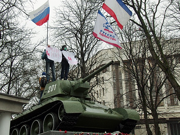 Grupo pró-Rússia sobre tanque soviético T-34 segura placa onde se lê 'Crimeia pela paz'  em frente ao Parlamento de Simferopol nesta sexta-feira (27). (Foto: Vasily Batanov/AFP)