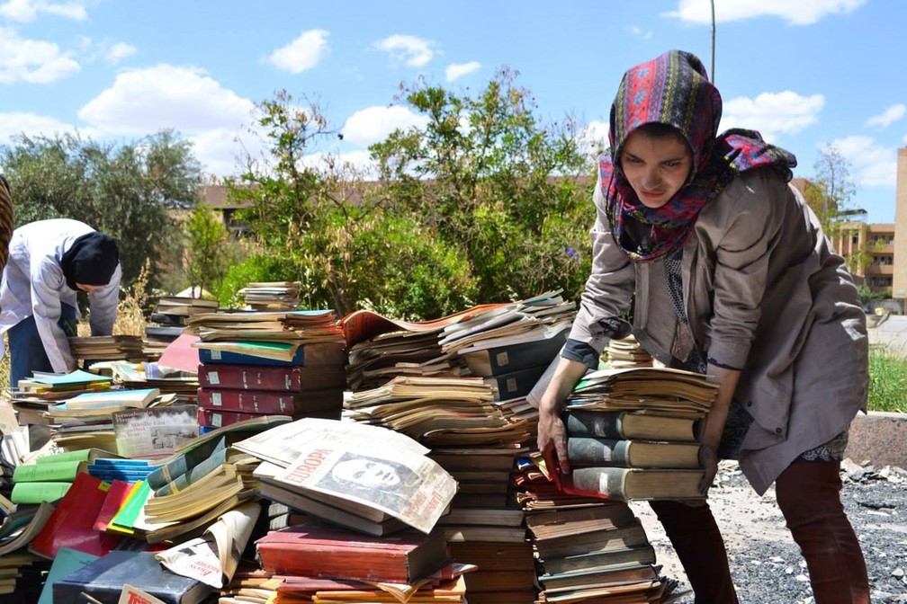 Voluntária de Mossul ajuda a empilhar os livros retirados da Biblioteca Central da Universidade de Mossul, após o Estado Islâmico deixar o prédio, depois de 19 meses usando a universidade como ponto militar estratégico (Foto: Ali Al-Baroodi)