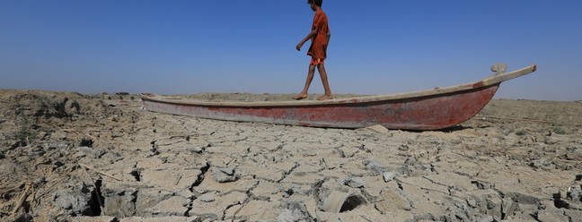 Um menino caminha perto de um barco deixado no leito seco de uma seção dos pântanos do sul do Iraque de Chibayish, na província de Dhi Qar. A seca no Iraque reflete um declínio no nível das vias navegáveis ​​devido à falta de chuva e fluxos mais baixos dos países vizinhos a montante, Irã e Turquia. — Foto: ASAAD NIAZI / AFP