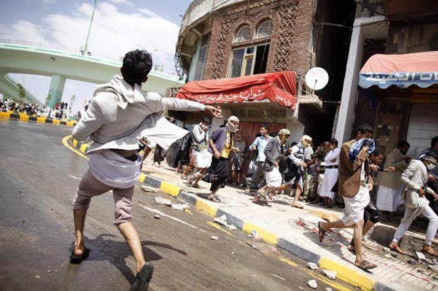 Manifestante joga pedra em policiais durante confronto próximo à Embaixada dos EUA no Iêmen, em Sanaa, nesta sexta-feira (14) (Foto: AFP)