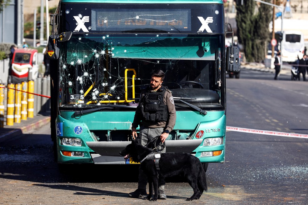 Um policial segura um cão de serviço perto de um ônibus danificado em Jerusalém — Foto: Ronen Zvulun/REUTERS