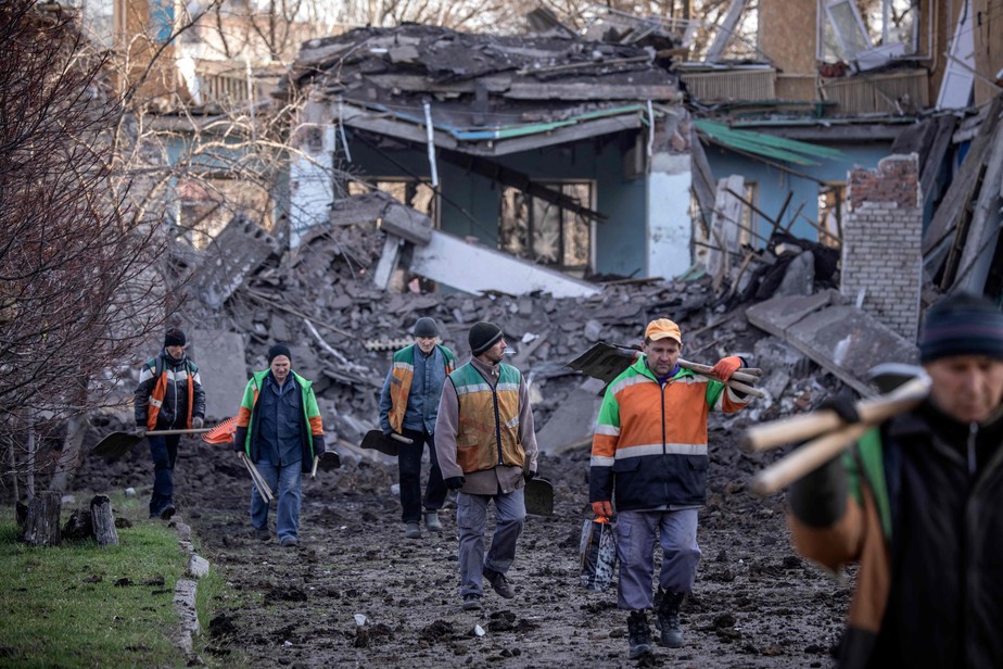 Trabalhadores da Defesa Civil ucraniana caminham ao lado de escola destruída em Kramatorsk