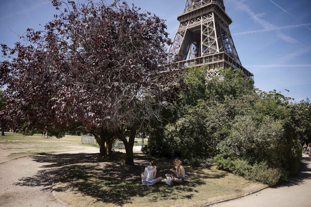Duas garotas fogem do calor em Paris ficando debaixo de árvore no Campo de Marte, próximo à torre Eiffel — Foto: Thomas Padilla/AP