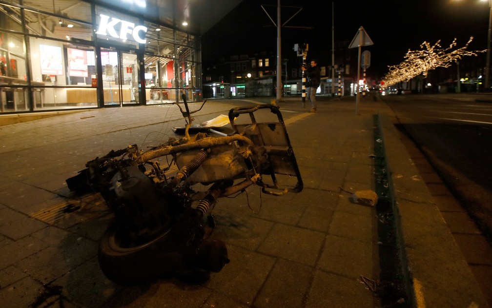  Restos de moto incendiada durante protesto contra toque de recolher em Roterdã, na Holanda, na segunda-feira (25) — Foto: AP Photo/Peter Dejong