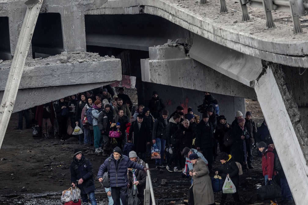 Refugiados atravessam uma ponte destruída em Irpin, cidade próxima a Kiev, capital da Ucrânia — Foto: REUTERS/Carlos Barria