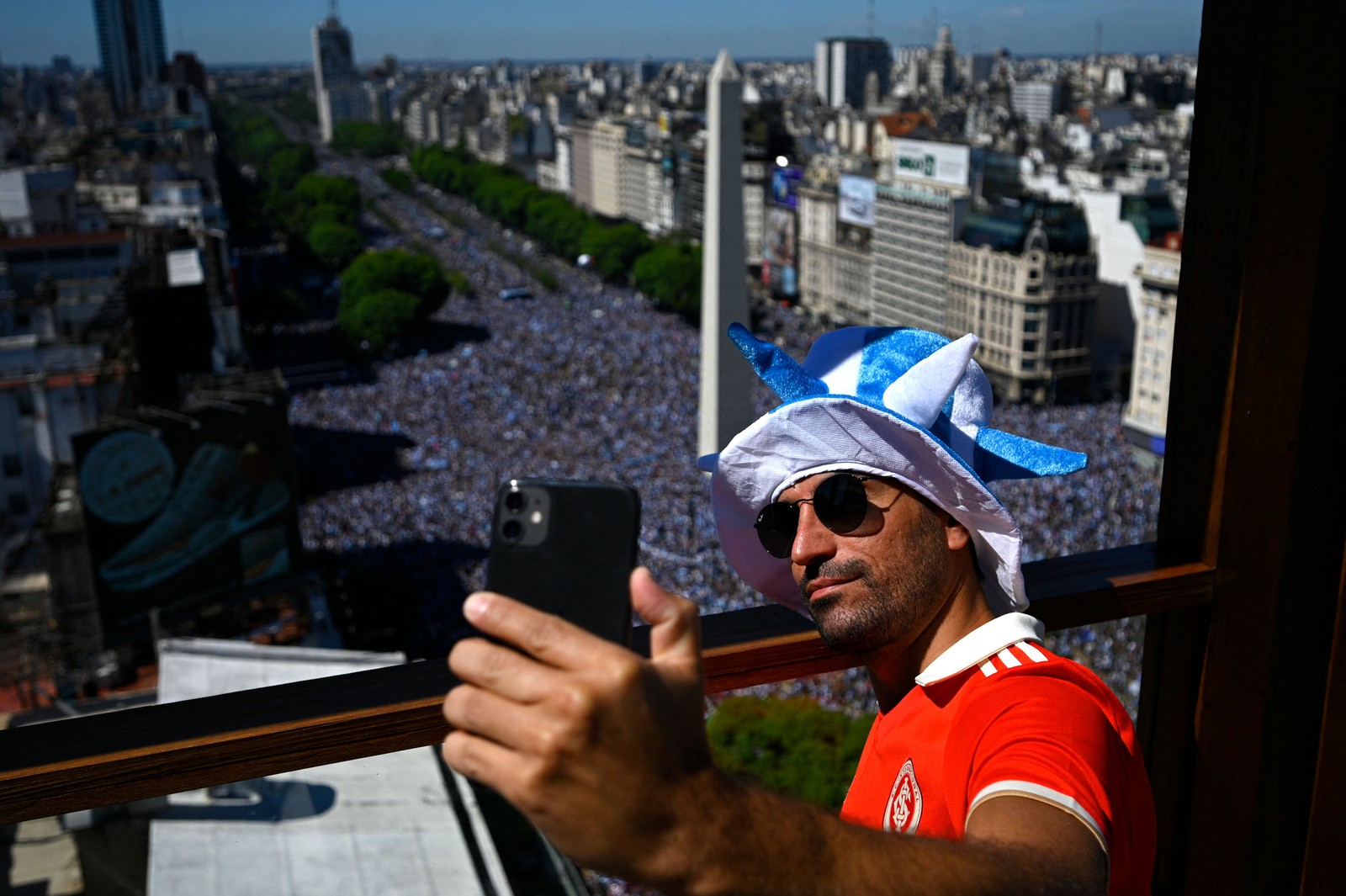 homem com a camisa do Internacional tira uma selfie perto do Obelisco, enquanto torcedores argentinos aguardam a passagem do ônibus com os jogadores da Argentina para comemorar a vitória na Copa do Mundo de 2022 — Foto: UIS ROBAYO / AFP