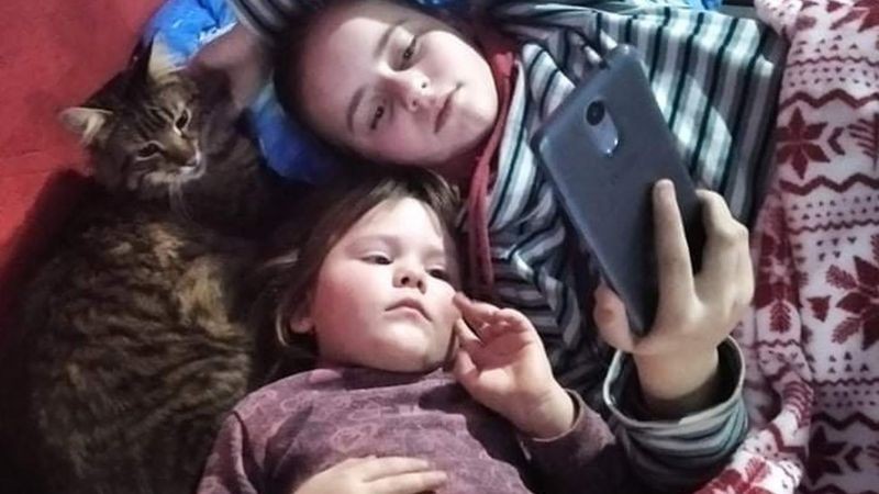 Filhas de Yuliia assistem a um vídeo no telefone de sua mãe (Foto: BBC News)