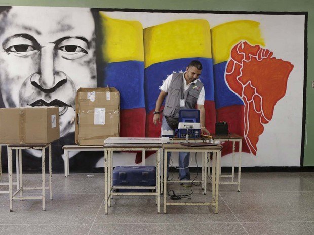 Funcionário do Conselho Eleitoral Nacional configura máquina de votação em frente a mural com a figura do ex-presidente Hugo Chávez em escola de Caracas (Foto:  REUTERS/Marco Bello )