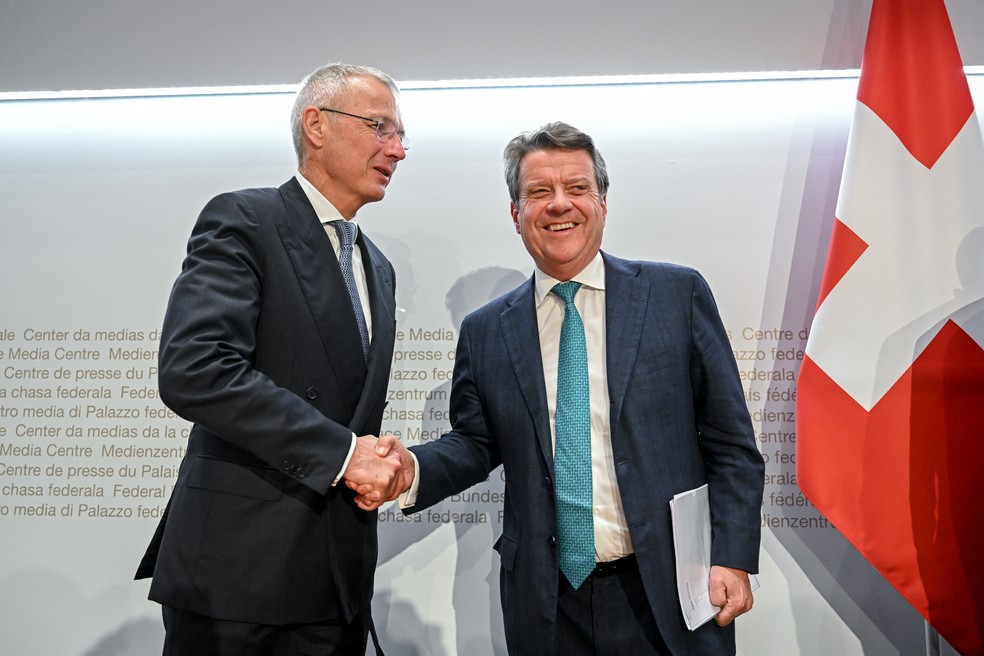 Foto tirada em 19 de março de 2023 em Berna, na Suíça, mostra o presidente do conselho de administração do Credit Suisse, Axel Lehmann (à esquerda), apertando a mão do presidente do conselho de administração do UBS, Colm Kelleher (à direita), logo após a entrevista coletiva na qual o UBS, maior banco suíço, anunciou a aquisição do segundo — Foto: Fabrice Cofrrini/AFP