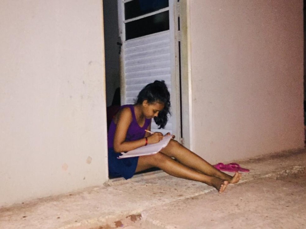 Sentada na porta de casa, Rafaele realiza as tarefas da escola   — Foto: Geovane Brito/G1