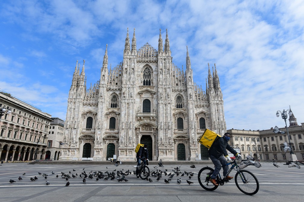 Ciclistas que trabalham com entrega de alimentos passam pela Piazza Duomo em Milão, na Itália, que estava deserta na terça-feira (31)  — Foto: Piero Cruciatti / AFP