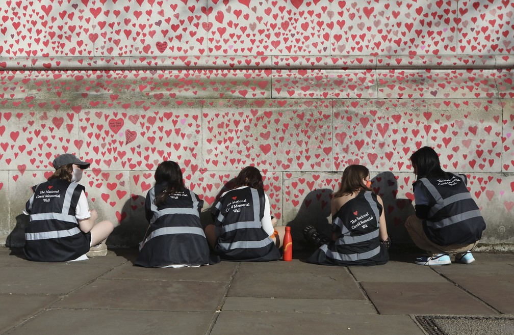Pessoas desenham corações no National Covid Memorial Wall, que está sendo pintado em memória das pessoas que morreram de coronavírus no Reino Unido — Foto: Luciana Guerra/PA via AP