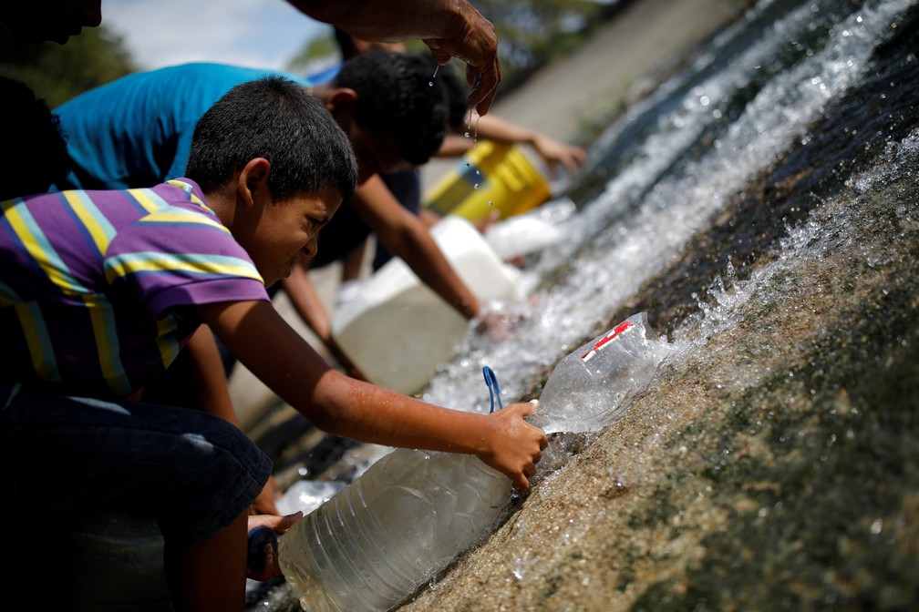 Criança capta água de esgoto que corre para o leito do Rio Guaire, em Caracas, notoriamente poluído.  — Foto: Reuters/Carlos Garcia Rawlins