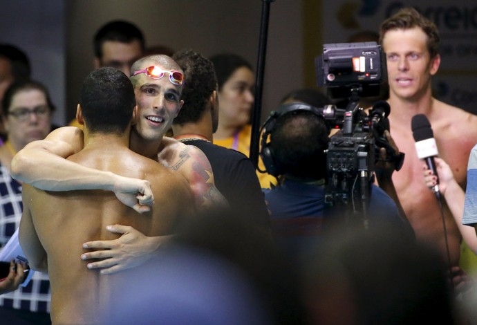 Bruno Fratus e Ítalo Manzine se abraçam enquanto Cesar Cielo concede entrevista (Foto: Reuters)