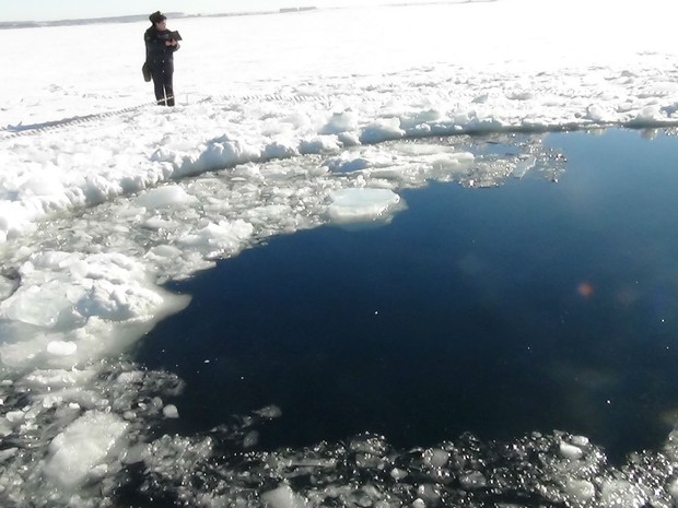 Pessoa pbserva buraco provocado por meteorito em lago congelado Chebarkul na Rússia. (Foto: AP)