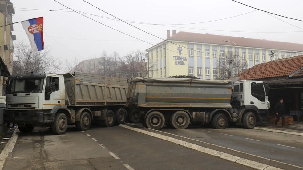 Uma barricada de caminhões carregados de pedra interrompe a passagem nessa rua de Mitrovica, ao norte do Kosovo. Tropas sérvia serão enviadas para a fronteira com a ex-província — Foto: AP - Bojan Slavkovic